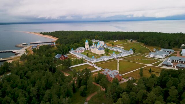 Epic remote island monastery aerial orbit. 
Cinematic 4K drone panorama of isolated 
historic christian fortress and ancient 
church inside vast northern forest.
