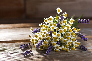 Fototapeta premium A bouquet of daisies and lavender rests on a rustic wooden surface.