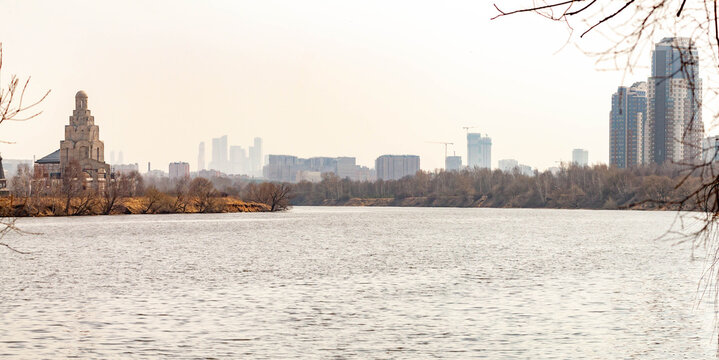 Scenic spring landscape in Strogino with Moskva River bend and Moscow City skyscrapers in a haze. Wide river view with residential district of Shchukino on a bright cloudy April day. Russia.