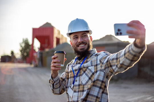 Engineer taking a selfie on a construction site, holding coffee and smiling, enjoying a break at work