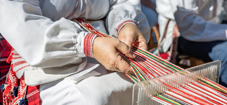 Process of weaving. Hands of a woman as they carefully manipulate colorful threads on a loom. Traditional clothing adds a touch of cultural significance, suggesting a connection to artisan skills.