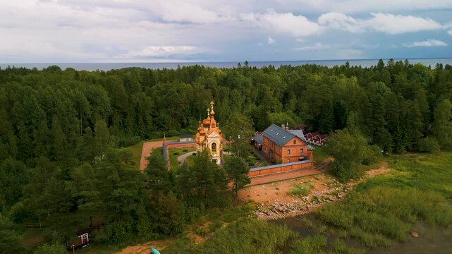 Aerial 180-degree orbit shot of a Russian Orthodox church with rising camera movement. Traditional architecture with copper domes at Lake Ladoga. 4K.