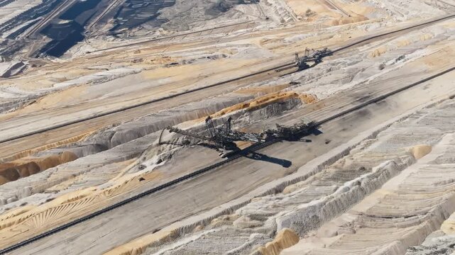 Aerial retreat of machinery in lignite coal mine in huge quarry, showing gathering of fossil fuel and recourses, pan up