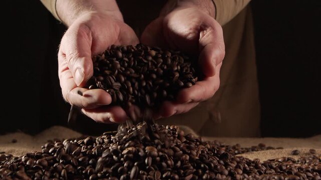 Slow motion of falling coffee beans from male hands on dark background. close-up