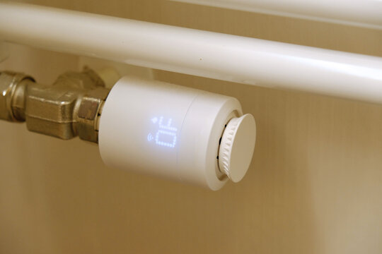 Modern smart thermostat head on white towel radiator in bathroom, white LCD screen showing temperature settings, hand adjusting dial. Energy saving, and modern climate control.