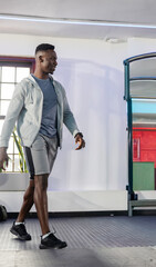 African American man walking across gym floor wearing light gray hoodie, gray shorts, smartwatch © wavebreak3