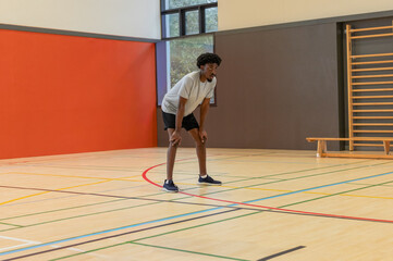 African American man in shorts bending and catching breath on gym court with multicolor lines © wavebreak3