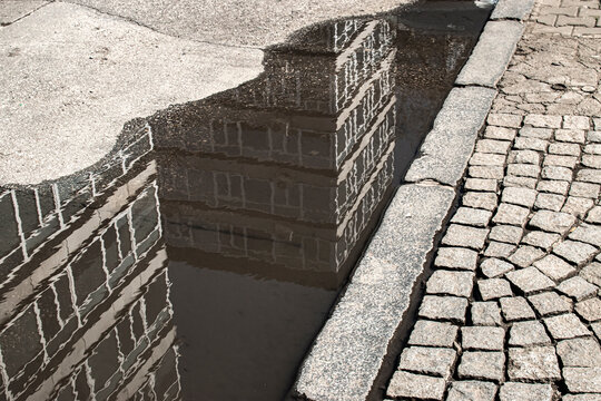 Abstract city reflection in puddle beside cobblestone pavement creating geometric urban composition