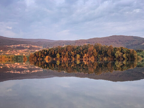 Golden hour reflection of a forested island in a tranquil river Minho with mountains, O Rosal, Galicia, Spain, March 2020