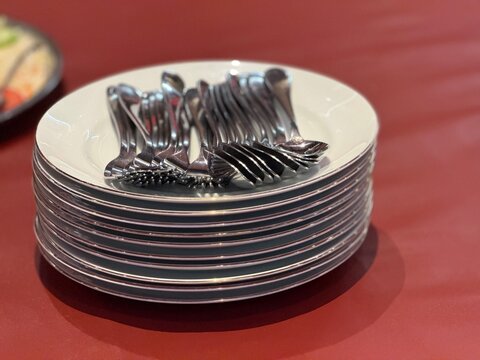 Neatly stacked plates and spoons prepared for catering service in Indonesia. Represents communal dining, events, and group meals such as gatherings, celebrations, or buka bersama. 
