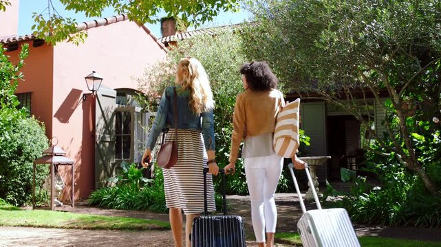 Friends, luggage and enter lodge outdoor for holiday destination, weekend getaway and sightseeing. Back, happy women and villa arrival with suitcase for vacation trip, scenery and countryside travel