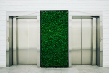 Wide shot of modern elevator lobby featuring green plant wall between lift doors, presenting sustainable office design concept. Supporting real estate, workplace branding, eco business marketing © Seventyfour