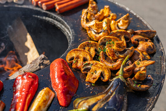 Variety of food being cooked on a grill. The food includes shrimp, corn on the cob, and flatbreads, which are all being cooked over an open fire. The food is being cooked in a round metal pan.