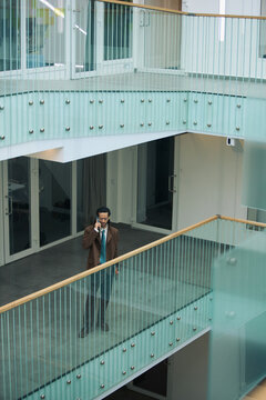 Vertical shot of middle aged businessman talking on smartphone while walking through modern office atrium, representing corporate communication and professional mobility for business marketing