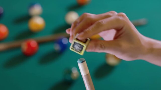 Billiard player rubs the end of the cue stick using special snooker chalk before billiards game important blow, standing in front of pool tables, sport activity at home indoors