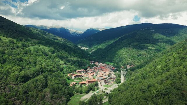 Drone orbit shot revealing Setcases mountain town surrounded by forest and valley landscape in Catalonia.