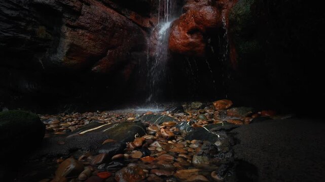 Tilt up shot from rocky stream bed to waterfall at Dicido Beach revealing wet cliffs, flowing water and vegetation above