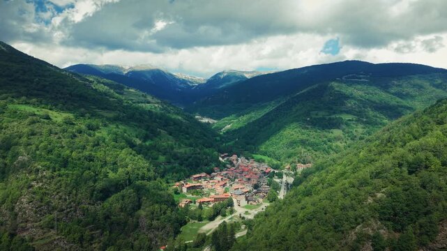 Drone moving forward into mountain valley revealing Setcases village surrounded by forest and clouds