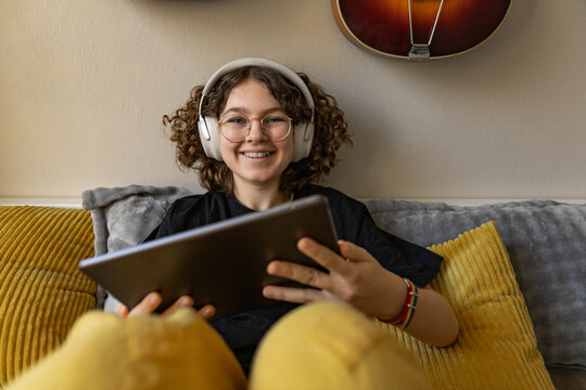 Smiling youth relaxing with headphones and tablet in cozy bedroom