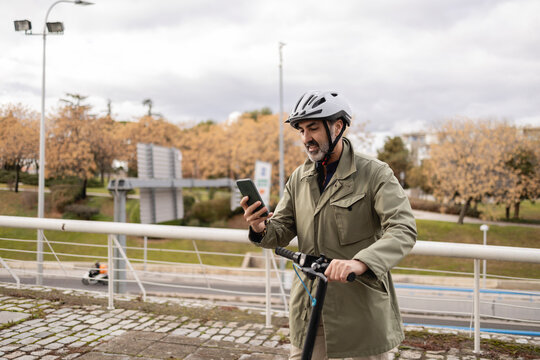 Man using phone while standing with scooter outdoors in city