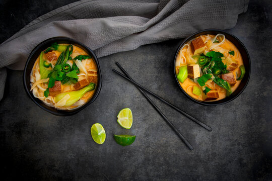 Red Thai curry soup with rice noodles smoked tofu and pak choi in bowls
