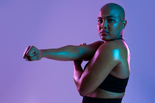Bald athlete in sportswear stretching arm in studio with purple background
