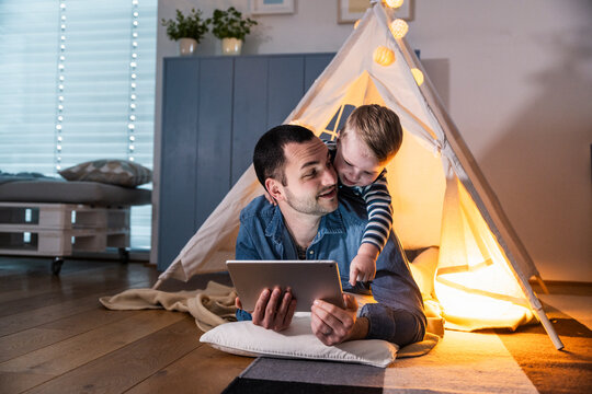 Father and son playing with tablet in cozy tent at home