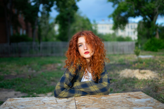 Red haired woman with curly hair in jeans outdoors at table