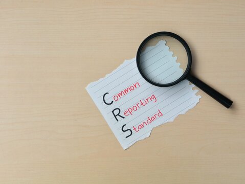Common reporting standard (CRS) text on a piece of paper with magnifying glass. Concept of financial transparency, international tax regulations, and global information exchange for tax purposes
