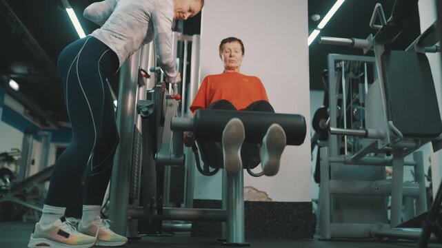 Senior woman exercising on leg extension machine with trainer