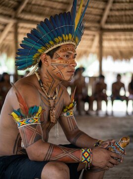 Indigenous man from the Brazilian Amazon with traditional adornments and body paint, in a community setting. Professional photograph, and cultural elements, with a blurred background.