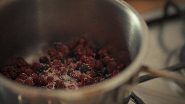 Housewife carefully stirs pot of homemade jam, crushing wild berries into fragrant, sweet preserve. In her kitchen she blends berries with sugar, showcasing cooking skill pleasure of fruit spreads