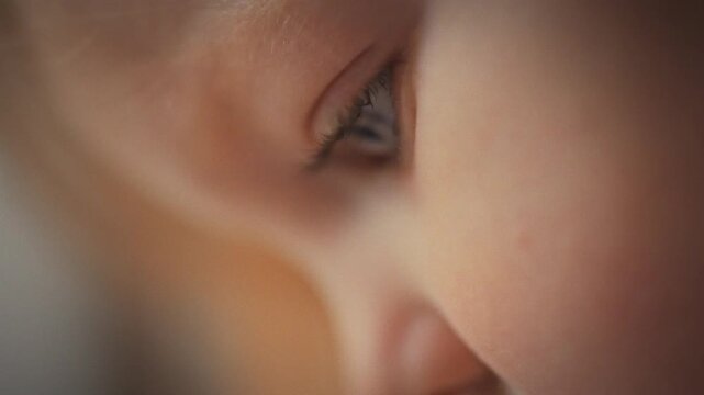 In softly lit studio, little girl's face dominates the frame, her eye shown in ultra-close-up, radiating focus. Gentle light highlights her smooth skin and bright iris, underscoring her concentration