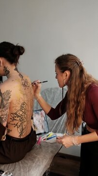 Close-up of a female tattoo artist draws a scketch of intricate floral and mandala design on a woman's upper back. Free hand tattoo technique.