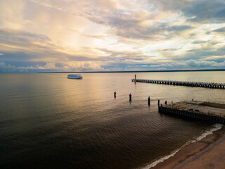 Fototapeta premium Aerial panoramic view of a cruise ship leaving the pier at sunset. Scenic northern lake coastline with cinematic sunset sky.