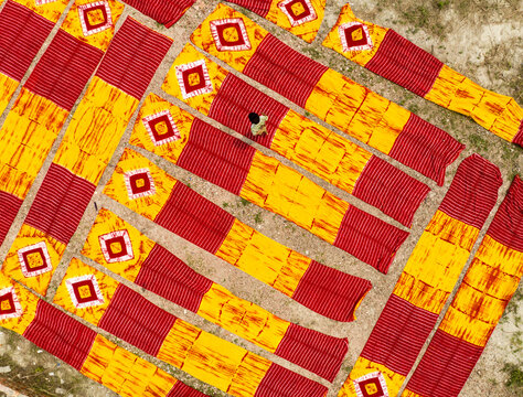 Narayanganj, Bangladesh - 30 March 2026: Aerial view of meticulously arranged textiles displaying vibrant patterns of red and yellow, creating a visually striking geometric landscape.