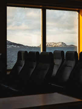 View of dark, plush seats lined up near a window overlooking the serene, snow-touched islands in the distance, Brensholmen, Troms, Norway.