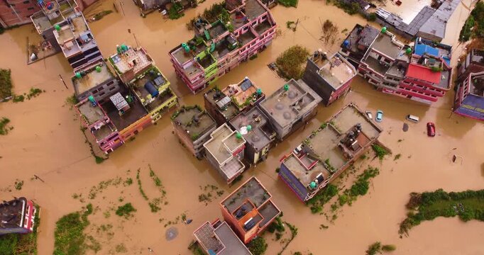 Top-down aerial drone shot of severe monsoon flooding in Banepa Nepal with residential buildings roads and numerous vehicles completely submerged under muddy water.