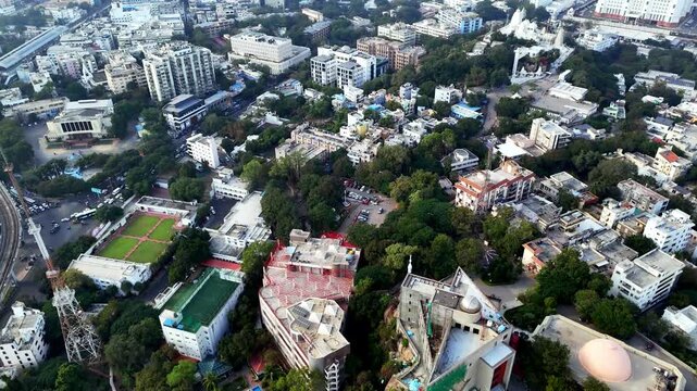 Drone shot capturing Hyderabad with compact housing clusters, commercial buildings, and road networks leading toward the elevated Birla Mandir nestled among lush green slopes.