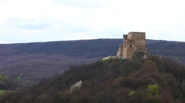 Distant view of the main tower of Csesznek Castle in Hungary rising above the forested hillside, showing medieval stone architecture, historic ruins and dramatic elevated landscape under cloudy sky