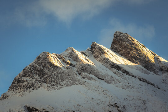 View of the majestic snow-capped mountain peaks kissed by sunlight against a backdrop of serene blue sky, Indregard, Troms, Norway.