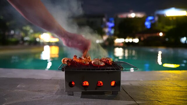 urban area. Grill seafood near pool in an hotel resort location. Smoke rises from the grill. Prepares shrimp grill on villa in tropical.