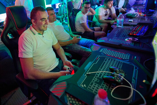 Group Of Friends Gaming Together At A Neon-Lit LAN Party With Controllers And PCs