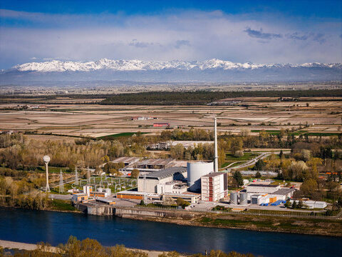 Trino, Italy - 30 March 2026: Aerial view of a decommissioned nuclear power plant stands against the backdrop of snow-capped mountains, where the river reflects the sky's azure hue.