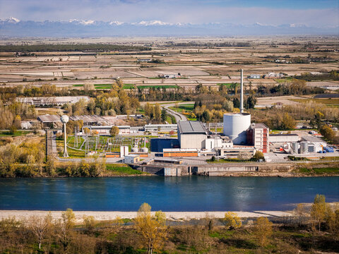 Trino, Italy - 30 March 2026: Aerial view of the Ex Centrale Nucleare, its stark white buildings contrasting against the deep blue river and distant snow-capped mountains.