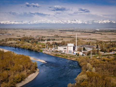 Trino, Italy - 30 March 2026: Aerial view of the Ex Centrale Nucleare di Trino, its structures rising against a backdrop of snow-capped mountains, bisected by the winding river.