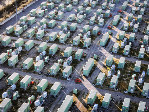 Trino, Italy - 30 March 2026: Aerial view of a sea of pale green containers neatly arranged in rows, casting long shadows on the dusty ground.
