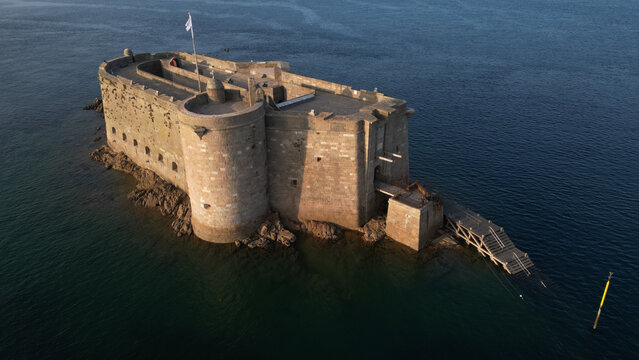 Aerial view of Fort du Taureau standing steadfast against the relentless sea, its ancient stone walls reflecting the golden light of the setting sun, Plouezoc'h, Bretagne, France.