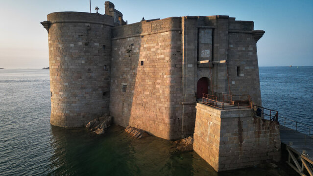 Aerial view of the imposing Chateau du Taureau fortress rises from the sea, its weathered stone reflecting the golden light of the setting sun, Plouezoc'h, Bretagne, France.