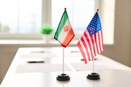 Flags diplomacy meeting on table symbolize negotiations. Iran and United States flags at conference table; dialogue, agreement, conflict. Represents international relations and strategic negotiation.